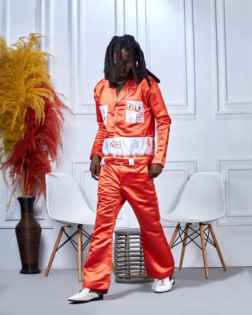 Man in an orange satin jacket and pants with printed patches, in a white studio